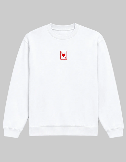 A white crewneck sweatshirt featuring a small red playing card (Ace of Hearts) graphic on the left chest, displayed against a clean white background.
